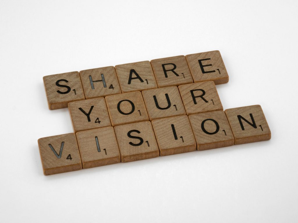 Scrabble tiles forming the inspiring phrase 'Share Your Vision' on a white background.