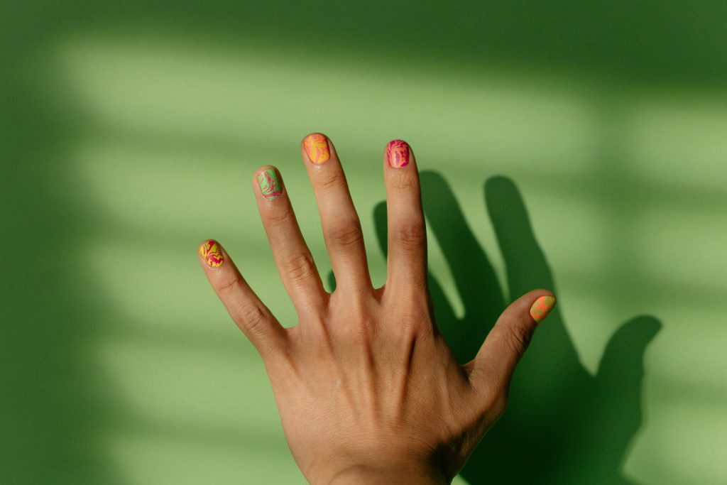 Close-up of a hand with intricate nail art casting shadows on a green surface.