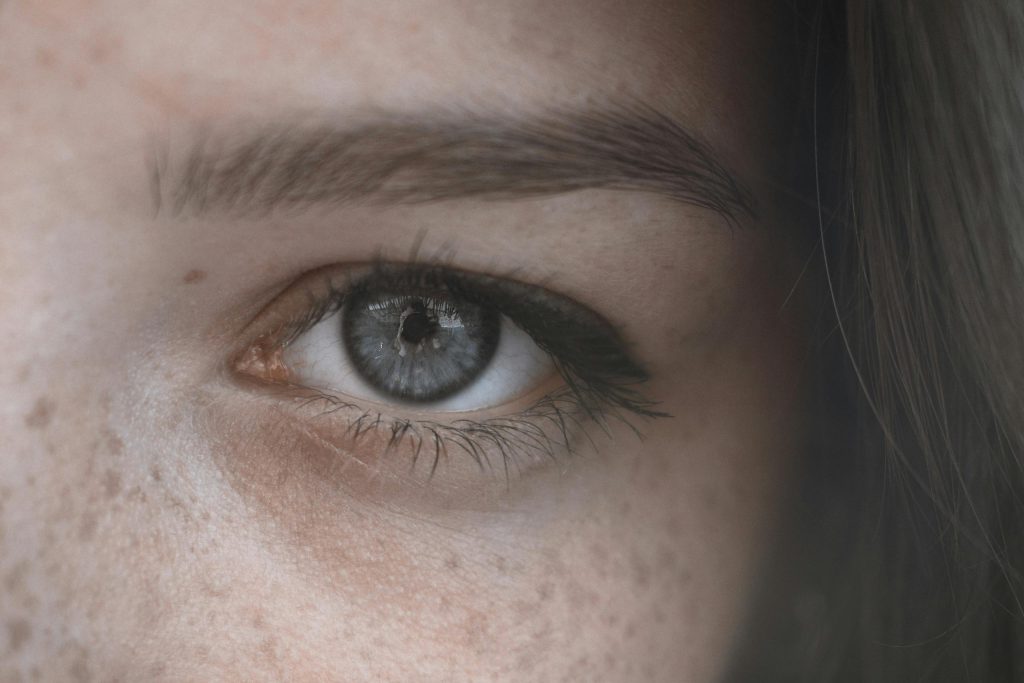 A detailed close-up of a blue eye surrounded by natural freckles and brows.