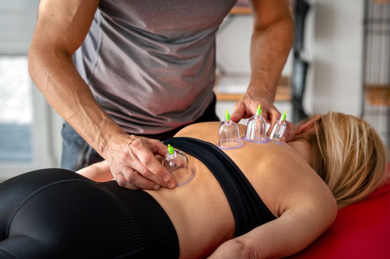 Sportski trener primjenjuje cupping tehniku na leđima klijentice kao dio oporavka nakon treninga
