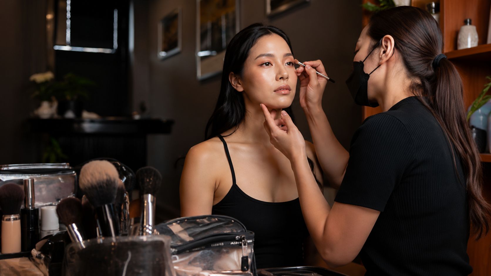 Vizažistica nanosi šminku modelu u kozmetičkom salonu, dok su u prvom planu kistovi i make-up pribor na stolu
