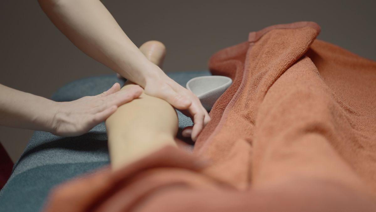 Ruke terapeuta masiraju nogu osobe koja leži prekrivena ručnikom tijekom tretmana tijela