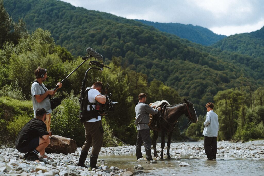 Film crew prepares horse while filming in a scenic mountainous valley setting.