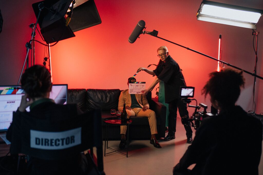 A behind-the-scenes look at a filming crew setting up a scene indoors with lighting equipment.