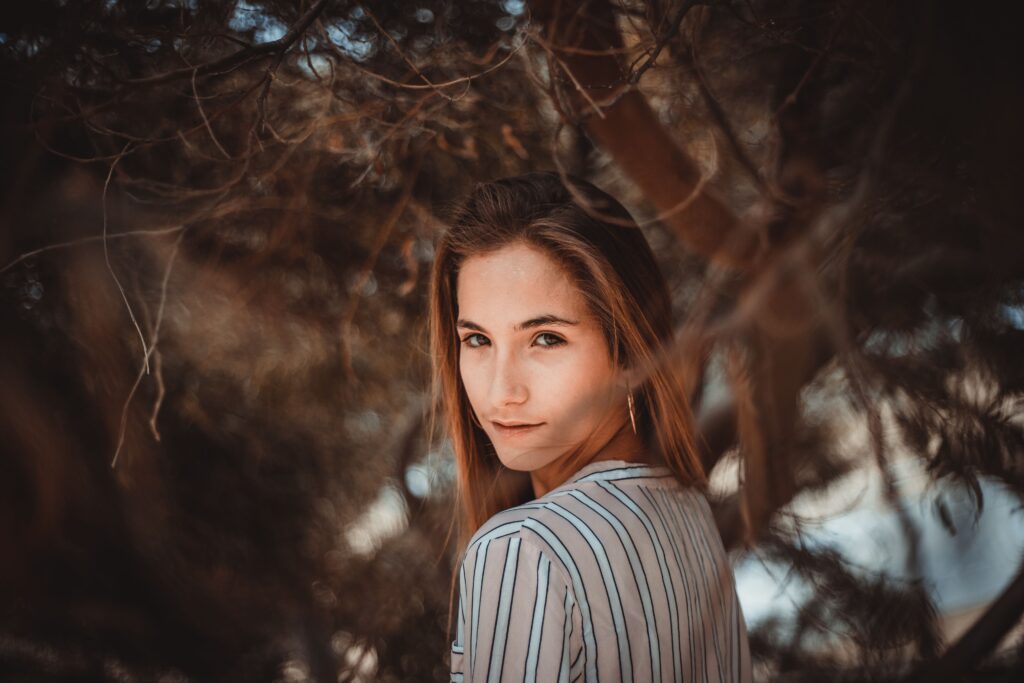 A woman in a striped shirt looking over her shoulder among tree branches, creating a moody and artistic portrait.