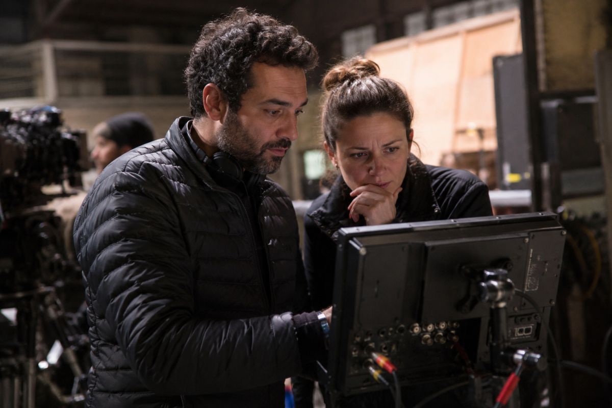 Filmski redatelj i producentica stoje uz monitor na filmskom setu i zajedno pregledavaju kadar, okruženi kamerom i produkcijskom opremom