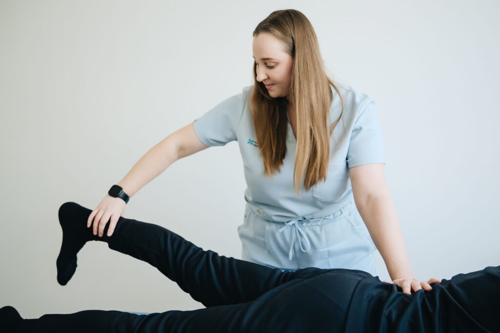 Female physiotherapist assisting patient in leg therapy session. Indoor clinical setting.