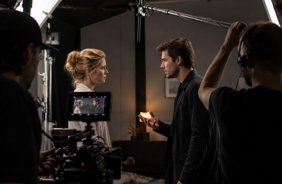 Filmski set tijekom snimanja dijaloške scene, s dvoje glumaca pred kamerom, rasvjetom, mikrofonom i članovima filmske ekipe