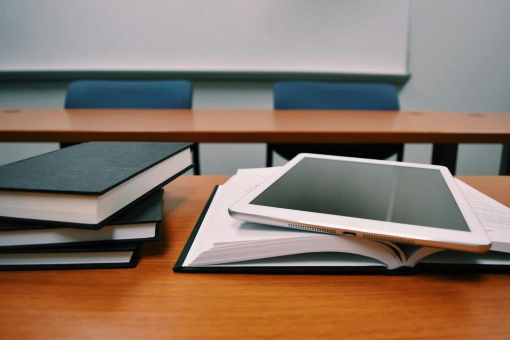 Knjige, otvoreni udžbenik i tablet na stolu u učionici za vrijeme obrazovanja i stručnog usavršavanja.
